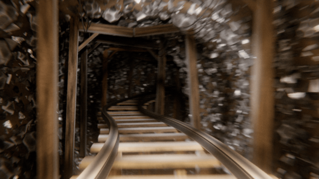 View of a curved and winding mine track inside a dimly lit tunnel, surrounded by rock walls.